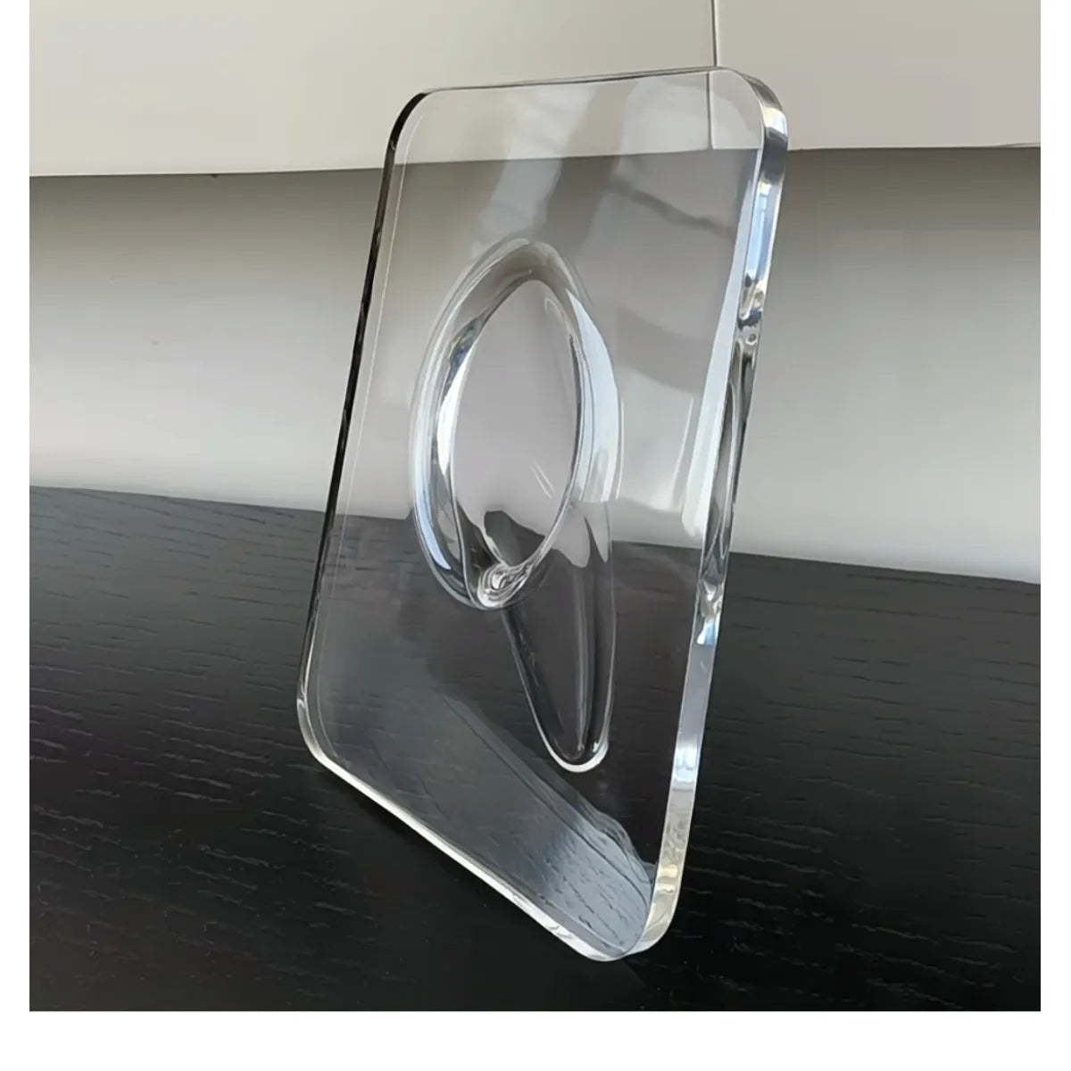 Clear acrylic frame vase with an oval flower opening, standing on a dark surface.
